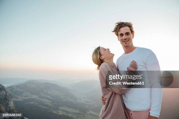 switzerland, grosser mythen, portrait of happy young couple standing in mountainscape at sunrise - auslachen blick in die kamera stock-fotos und bilder