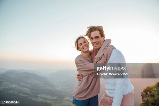 switzerland, grosser mythen, portrait of happy young couple hugging in mountainscape at sunrise - mann lachen blick in die kamera stock-fotos und bilder