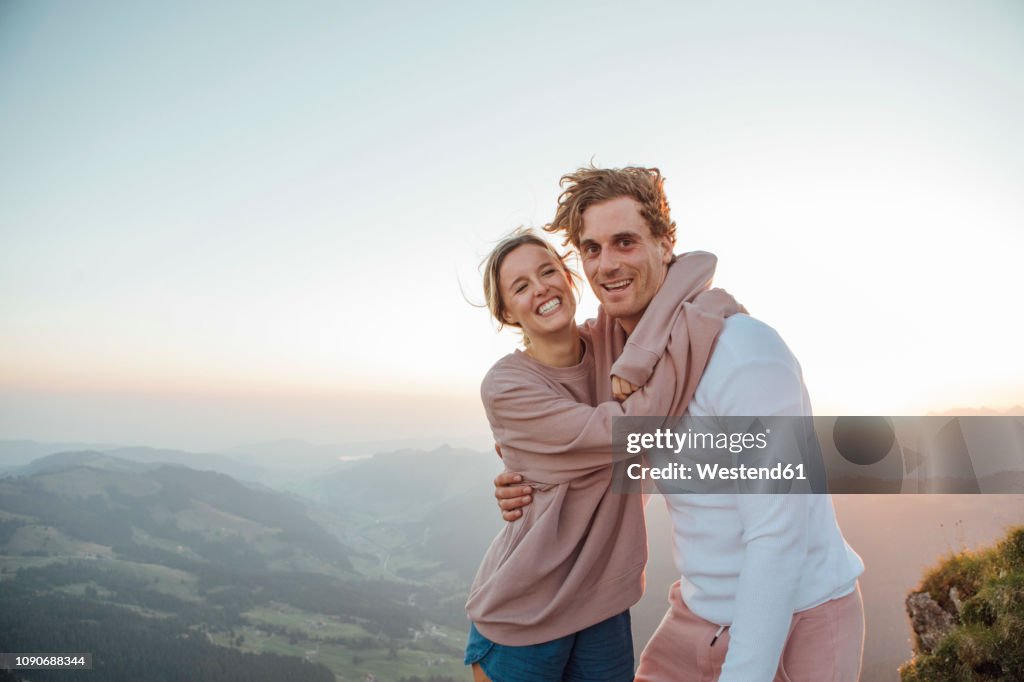Switzerland, Grosser Mythen, portrait of happy young couple hugging in mountainscape at sunrise