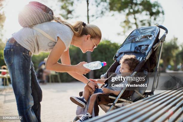 mother giving water bottle to his son, sitting in pram - mother stroller stock pictures, royalty-free photos & images