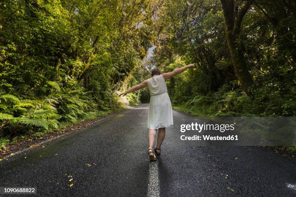 new zealand, north island, egmont national park, woman balancing on centre line on road - new zealand leaves stockfoto's en -beelden