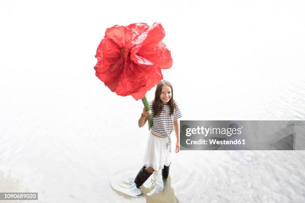 portrait of smiling girl standing in a lake holding oversized red artificial flower - long stem flowers fotografías e imágenes de stock