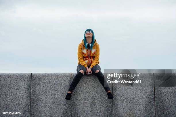 young woman with dyed blue hair sitting on a wall looking up - people revolutionary front stock-fotos und bilder