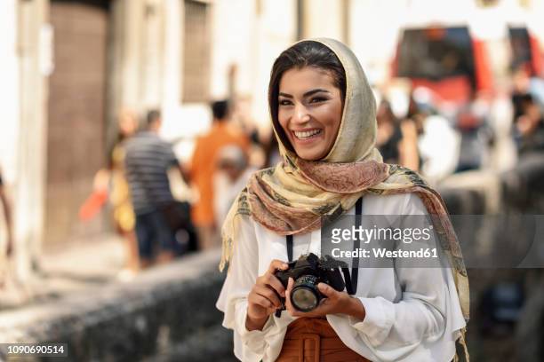 spain, granada, young arab tourist woman wearing hijab, using camera during sightseeing in the city - arab people laugh stockfoto's en -beelden