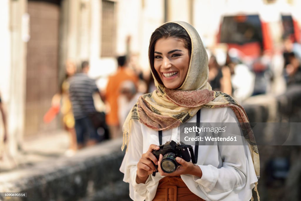 Spain, Granada, young Arab tourist woman wearing hijab, using camera during sightseeing in the city