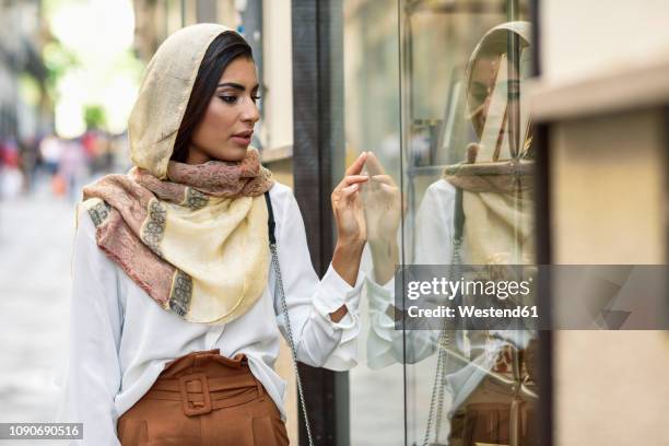 spain, granada, young muslim tourist woman wearing hijab looking at shop windows on a shopping street - arab culture stock pictures, royalty-free photos & images