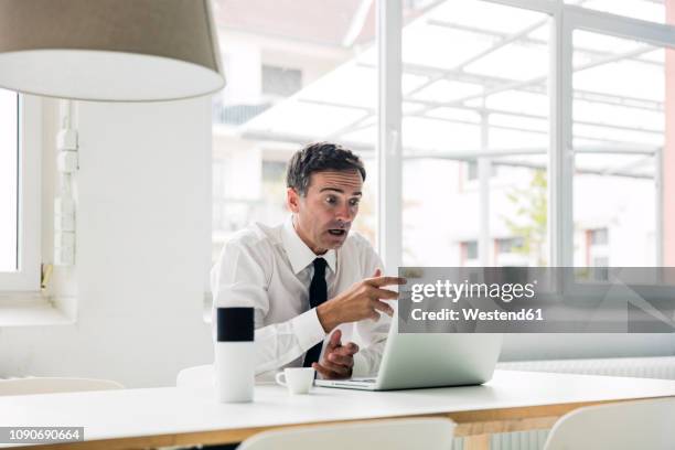 shocked businessman looking at laptop on table in office - terrified stock pictures, royalty-free photos & images