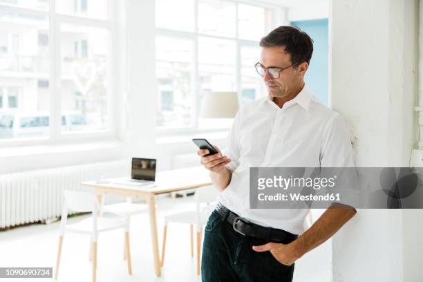 businessman looking on cell phone in bright office - geschäftsmann im büro mobiltelefon stock-fotos und bilder