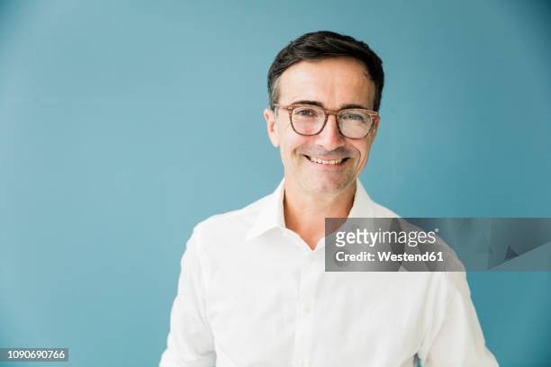 portrait of smiling businessman wearing glasses - blue background portrait bildbanksfoton och bilder
