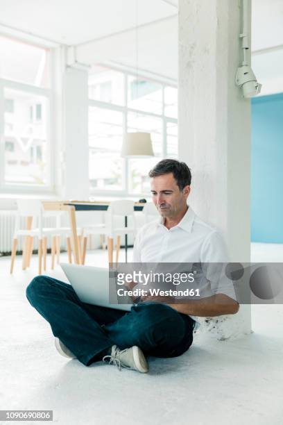 businessman sitting on the floor in office using laptop - schneidersitz stock-fotos und bilder
