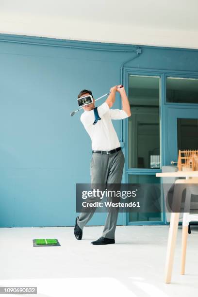 businessman wearing vr glasses playing golf in office - golf player stockfoto's en -beelden