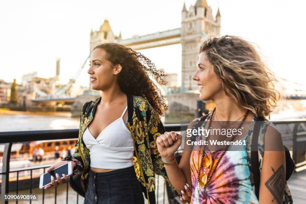 uk, london, two friends together in the city with tower bridge in background at sunset - london fashion stock-fotos und bilder