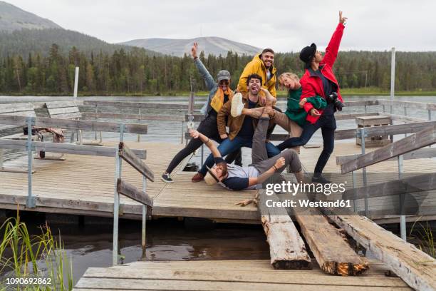 finland, lapland, portrait of happy playful friends posing on jetty at a lake - finnland fotografías e imágenes de stock