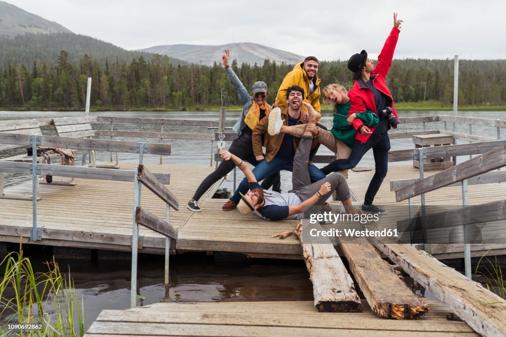 Finland, Lapland, portrait of happy playful friends posing on jetty at a lake