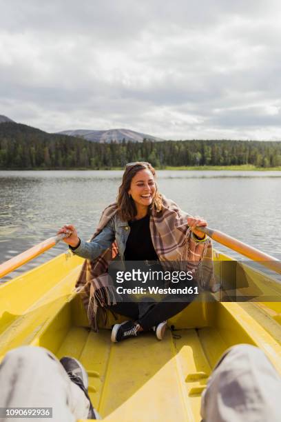 finland, lapland, laughing woman wearing a blanket in a rowing boat on a lake - finnland stock-fotos und bilder