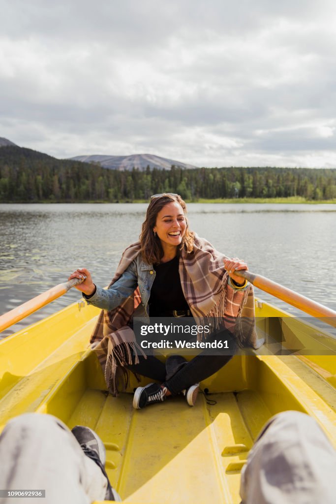 Finland, Lapland, laughing woman wearing a blanket in a rowing boat on a lake