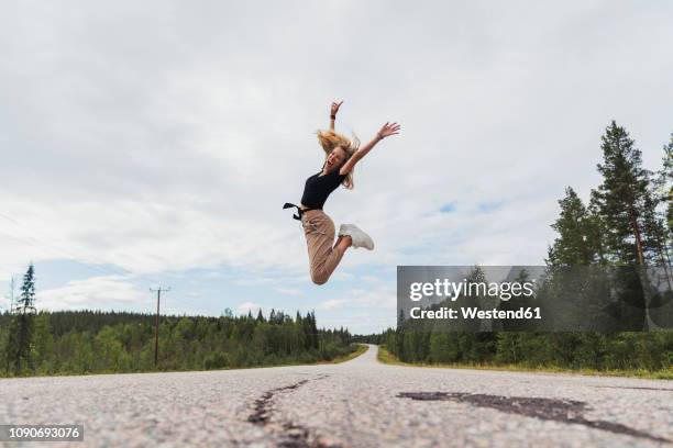 finland, lapland, exuberant young woman jumping in rural landscape - finland women stock pictures, royalty-free photos & images