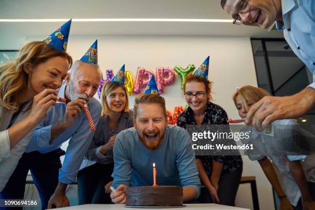 colleagues having a birthday celebration in office with cake, party blower and party hats - happy birthday written imagens e fotografias de stock