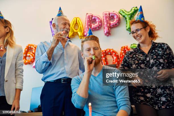 colleagues having a birthday celebration in office with party blower and party hats - party blower stock-fotos und bilder