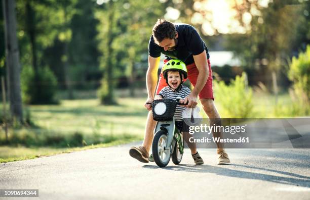 father teaching little son riding bicycle - sportschutzbekleidung stock-fotos und bilder