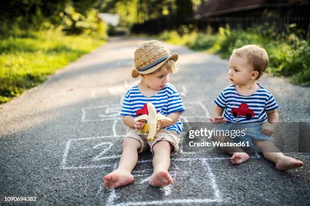 toddler boy and his little sister sitting together on the street eating bananas - jealous sister stock pictures, royalty-free photos & images