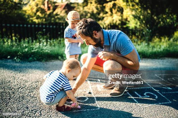 father drawing hopscotch on asphalt - hopscotch stock pictures, royalty-free photos & images