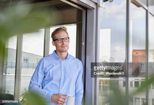 young man with cup of coffee standing at balcony door - townhouse stock-fotos und bilder