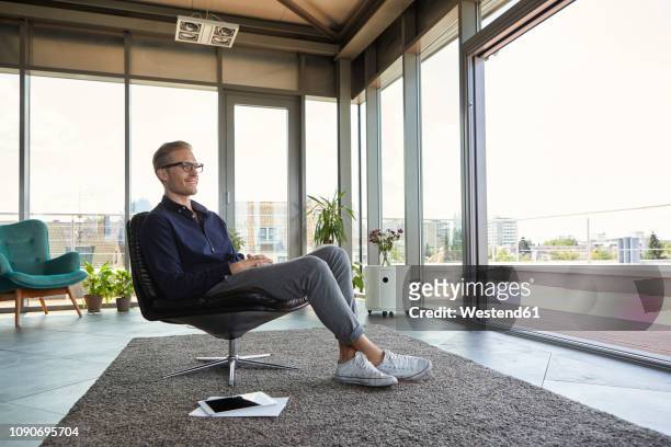 smiling young man sitting in armchair at the window at home - entry draft portraits bildbanksfoton och bilder