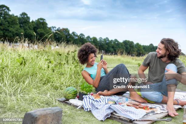 happy couple having a barbecue and taking cell phone pictures in the nature - paar picknick stock-fotos und bilder