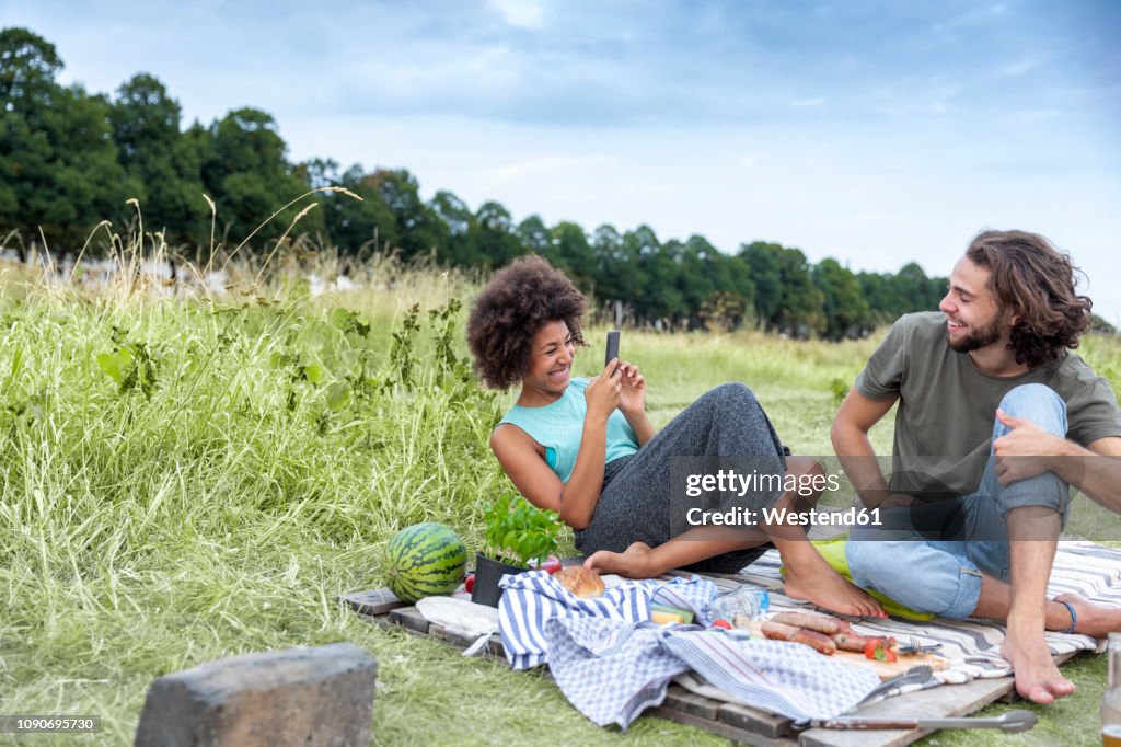 Happy couple having a barbecue and taking cell phone pictures in the nature
