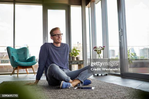 smiling young man sitting on carpet with tablet at home - sitting on ground stock pictures, royalty-free photos & images