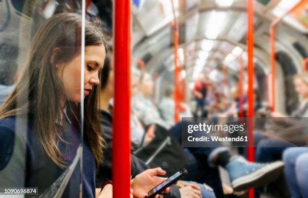 uk, london, young woman in underground train looking at cell phone - london tube stock-fotos und bilder