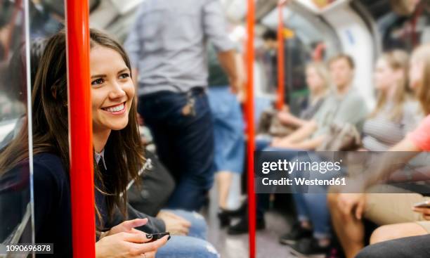 uk, london, portrait of smiling woman with cell phone sitting in underground train - london tube stock-fotos und bilder