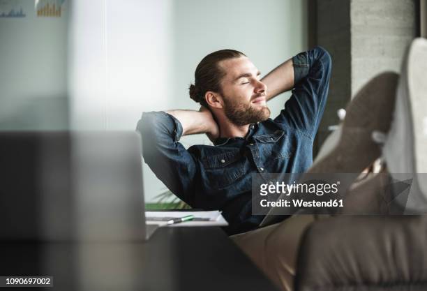 relaxed smiling businessman sitting in office with closed eyes - contento foto e immagini stock