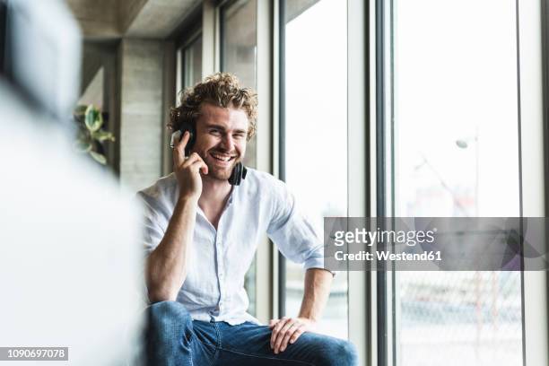 happy casual young man listening to music with headphones at the window - in den zwanzigern stock-fotos und bilder