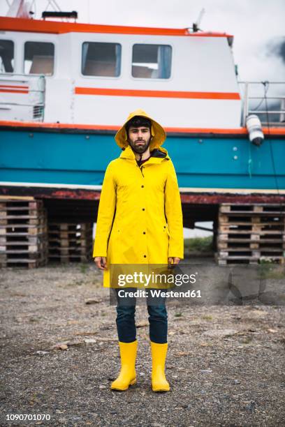 young man standing in front of a ship, wearing rain clothes, lapland, norway - レインコート ストックフォトと画像