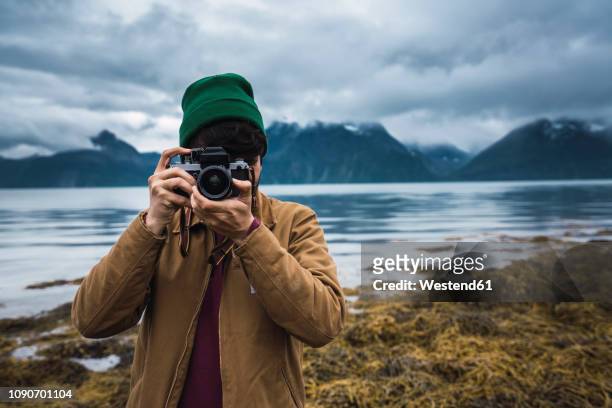 young man with woolly hat taking pictures with camera - photographer stock-fotos und bilder