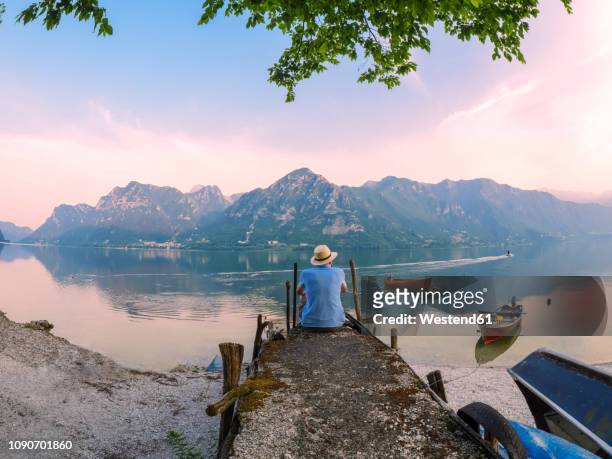 italy, lombardy, back view of man sitting on jetty at lake idro at morning twilight - westend 61 fotografías e imágenes de stock