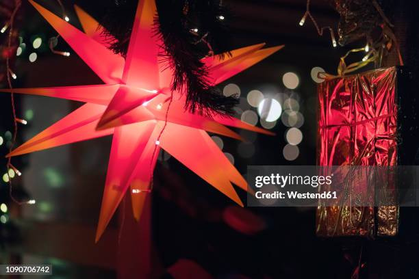 lighted red moravian star and gleaming red christmas present - herrnhuter stern stock-fotos und bilder