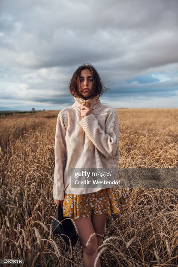 Portrait of young woman wearing oversized turtleneck pullover standing in corn field