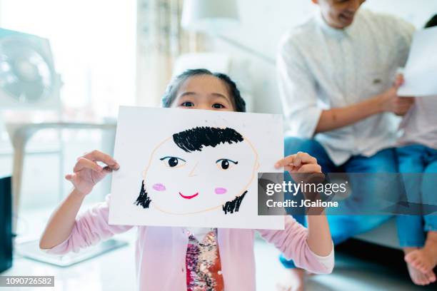 young girl holding a self drawn portrait in front of her face - self portrait stock pictures, royalty-free photos & images