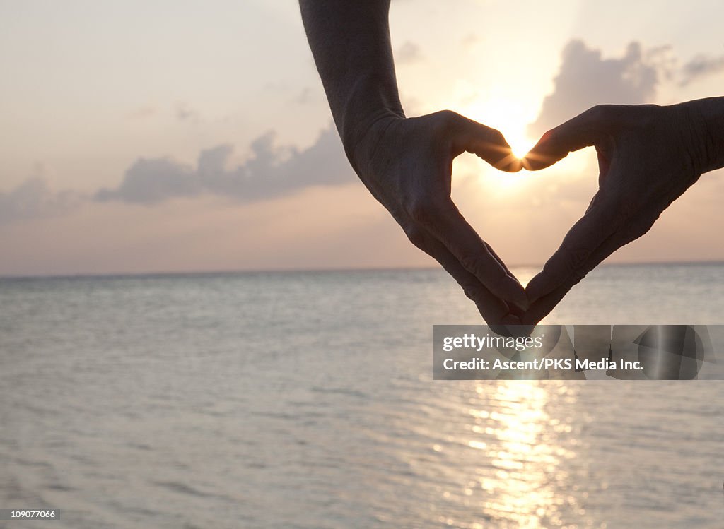 Detail of woman's hands making heart shape, sea