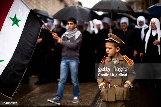 Druze boy wears a Syrian army uniform as men walk with Syrian flags during a rally at the village of Majdel Shams near the border between Israel and...