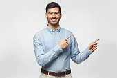 Smiling businessman pointing right with two hands and looking at camera, isolated on gray background