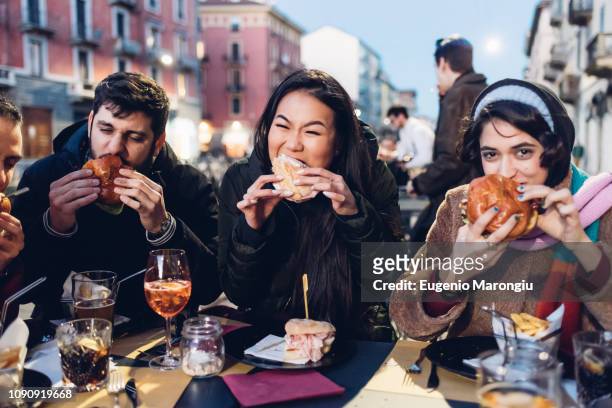 friends enjoying burger at outdoor cafe, milan, italy - milan italy stockfoto's en -beelden
