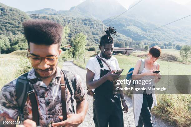 young adult hikers on rural dirt track looking at smartphones,  primaluna, trentino-alto adige, italy - jeans latzhose frau stock-fotos und bilder