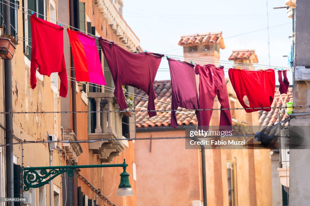 Red and pink clothing on clothesline outside traditional houses, Venice, Veneto, Italy