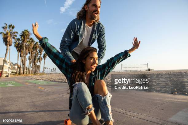 feliz pareja patinaje en venice beach - california - venice california fotografías e imágenes de stock