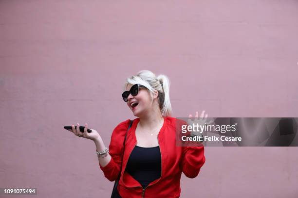 a young lady having phone in her hand and doing hand gestures against a pink background - smart casual stock pictures, royalty-free photos & images