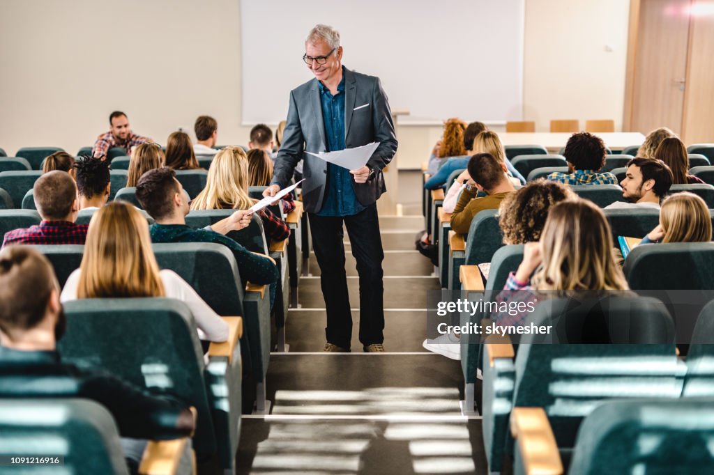 Heureux homme professeur donnant des résultats de test de ses étudiants en amphithéâtre.